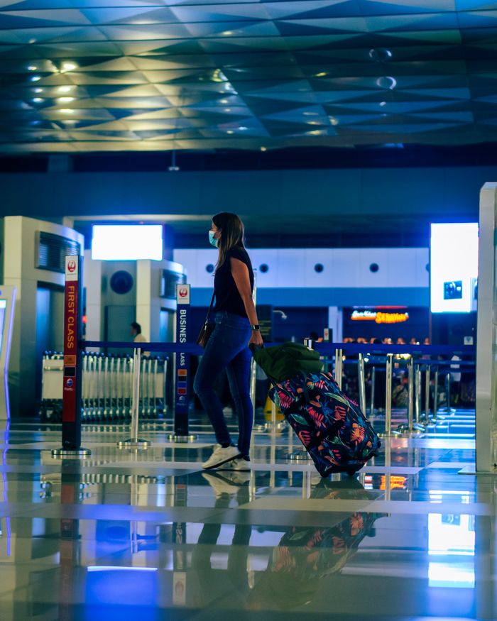 A woman wearing a face mask walks through an airport with luggage, reflecting modern travel trends.
