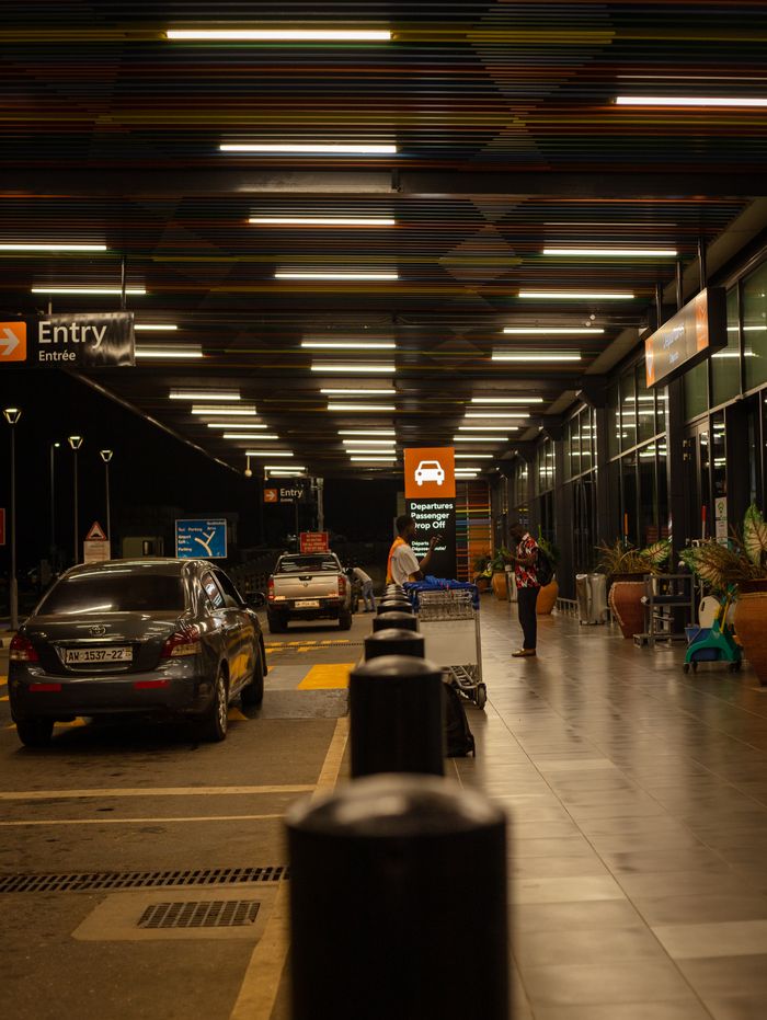A nighttime view of an airport drop-off zone featuring parked cars and passengers.